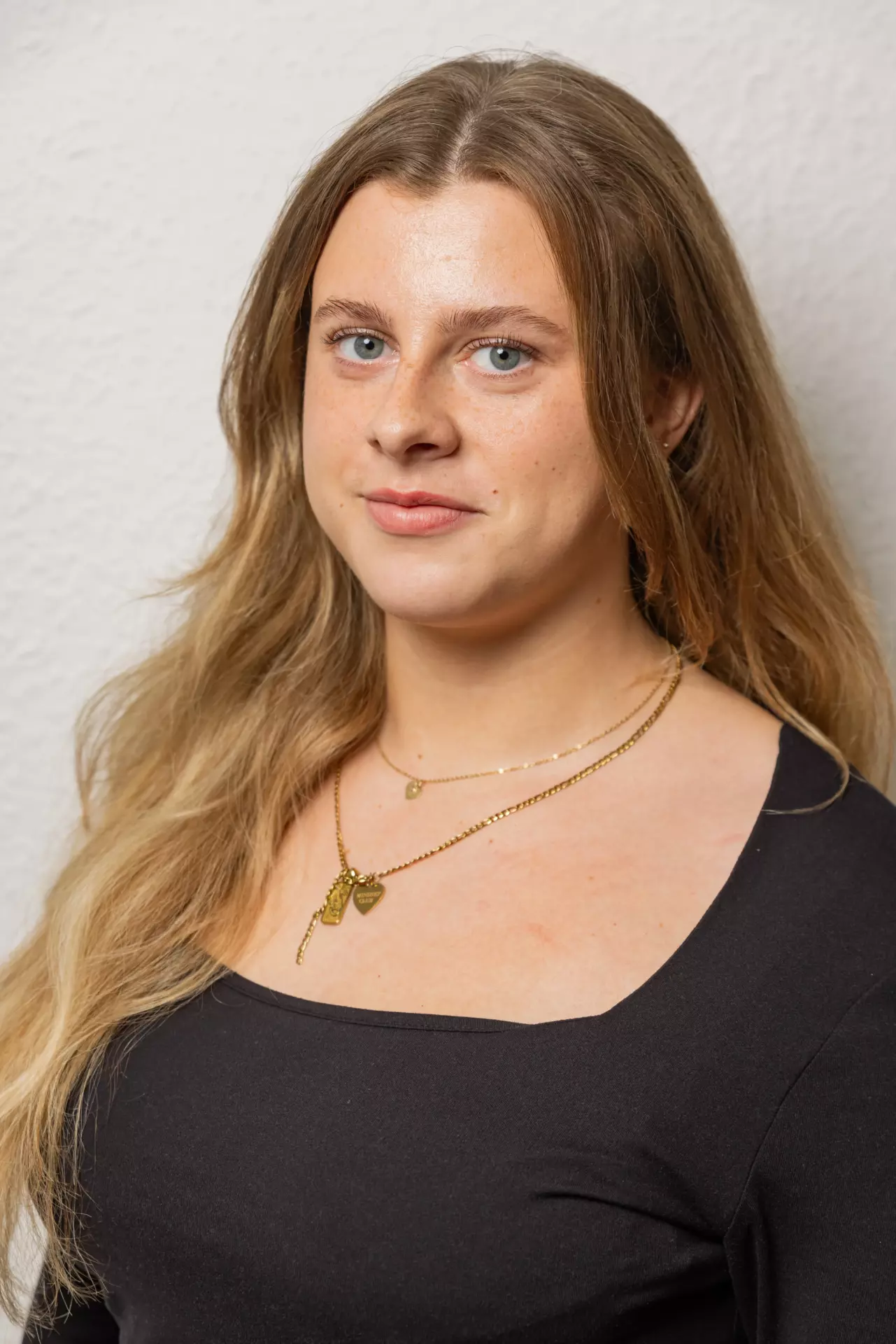 Porträt einer Frau mit langen blonden Haaren, die einen schwarzen Pullover trägt und zwei goldene Ketten.