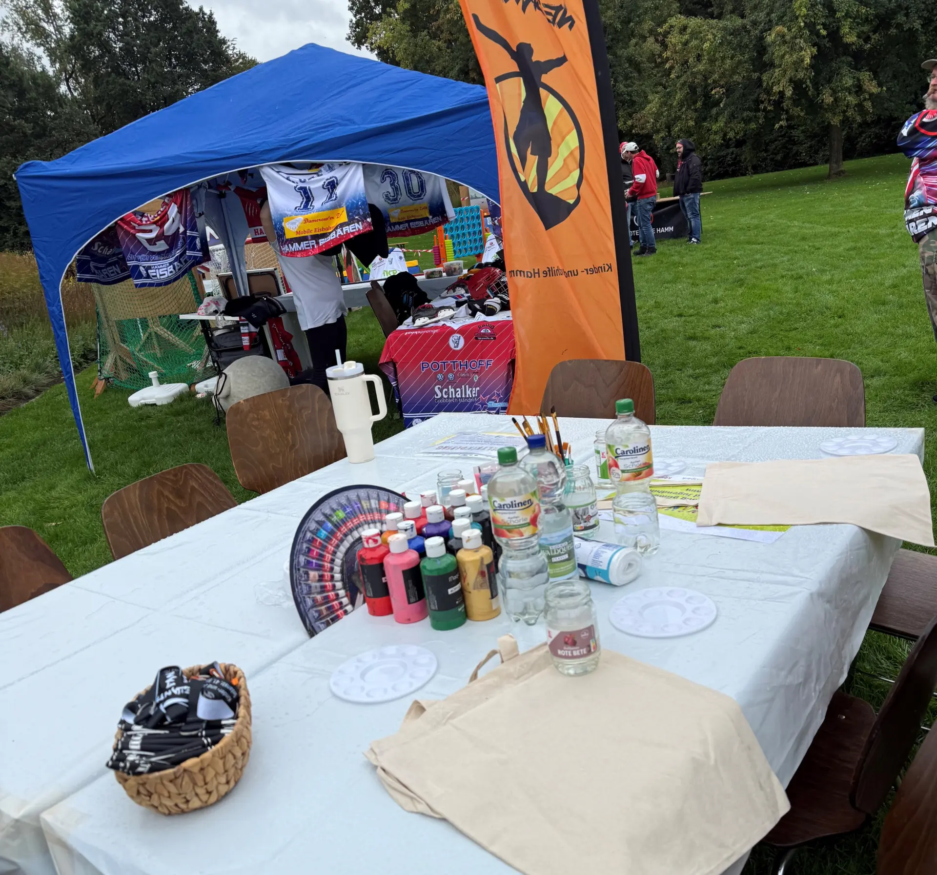 Ein Tisch mit verschiedenen Farben, Pinsel, und Bastelmaterialien auf einem weißen Tuch.