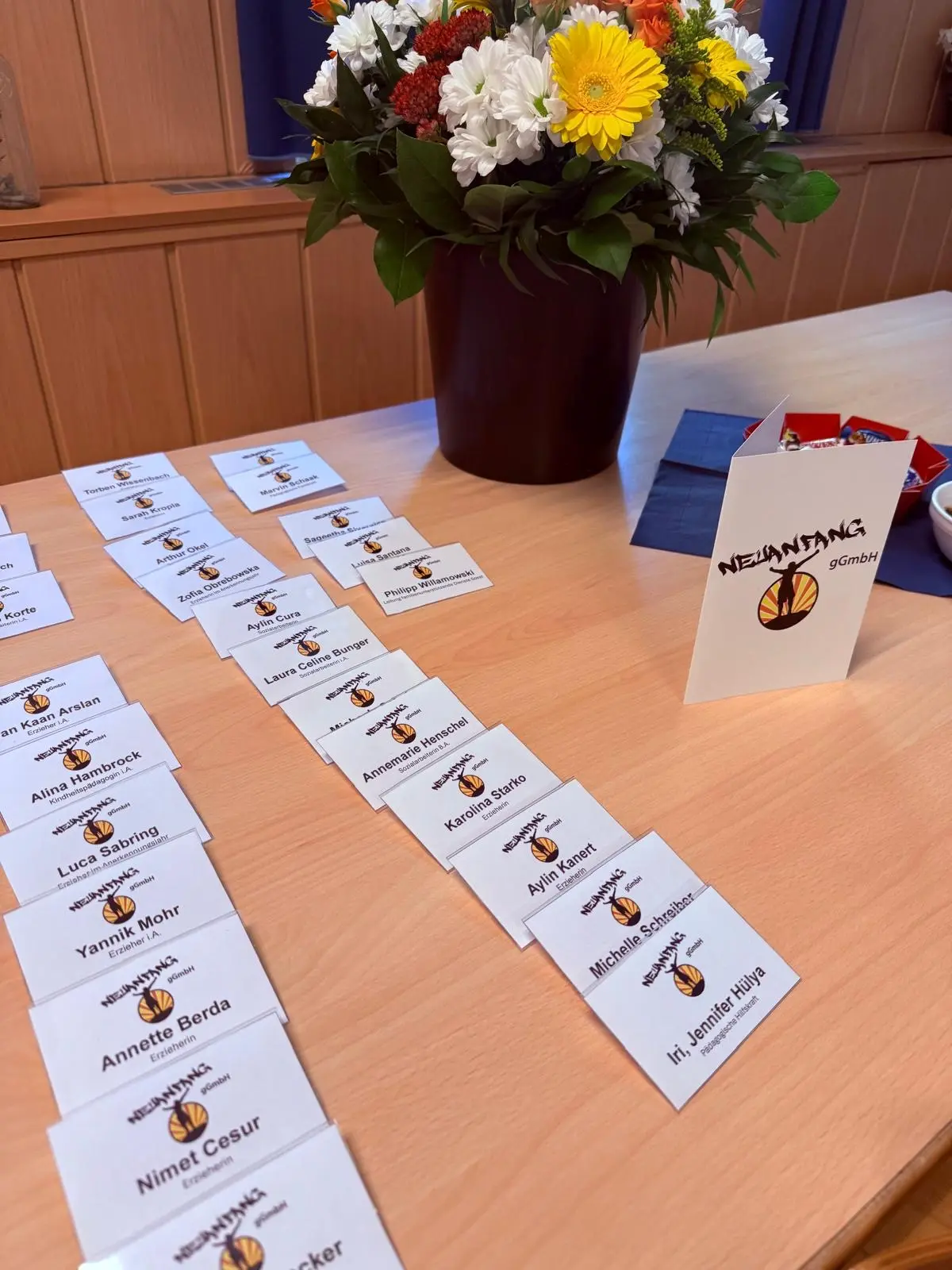 erfolgreiche_abschluesse Reihe von Namensschildern auf einem Tisch, mit einem Blumenarrangement im Hintergrund.