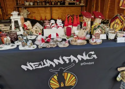 Tisch mit verschiedenen Weihnachtsdekorationen, Kerzen und handgefertigten Artikeln, dekoriert mit dem Logo von Neuanfang gGmbH.