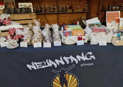 Tisch mit verschiedenen handgefertigten Produkten und Geschenken, präsentiert auf einem Weihnachtsmarktstand von Neuanfang gGmbH.