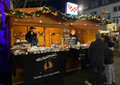 Zwei Verkaufsstände auf einem Weihnachtsmarkt mit handgefertigten Produkten und dekorativen Lichtern. Stände repräsentieren die Organisation Neuanfang Hamm.