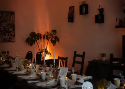 Tisch gedeckt mit Tellern, Tassen und Dekoration für ein festliches Abendessen in einem gedämpften Lichtambiente.