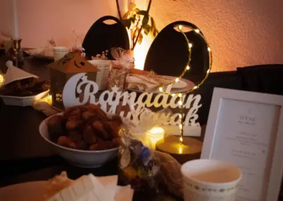Tischdekoration mit einem Schriftzug 'Ramadan Mubarak', Datteln in einer Schüssel und festlicher Beleuchtung.