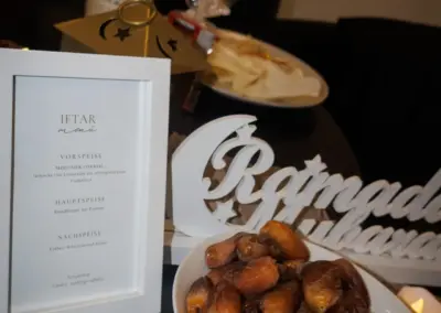 Schüssel mit Datteln auf einem Tisch, umgeben von einem Menü für ein Iftar-Essen und Dekorationen.