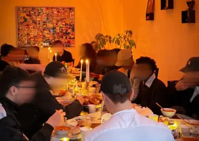 Tisch mit mehreren Personen, die gemeinsam eine Mahlzeit einnehmen, umgeben von Kerzenlicht und dekorativen Elementen.