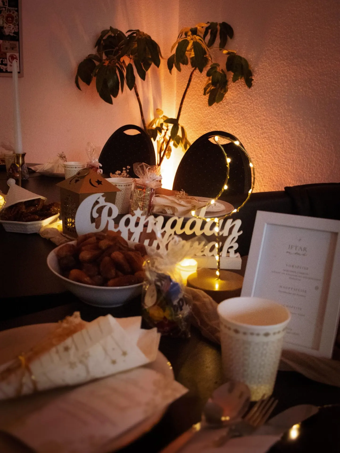Tischdekoration mit einem Schriftzug 'Ramadan Mubarak', Datteln in einer Schüssel und festlicher Beleuchtung.