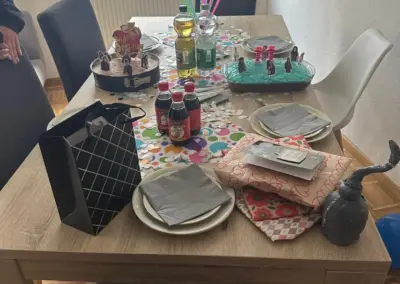 Bunt gedeckter Holztisch mit Kuchenfiguren, Getränken, Konfetti, Geschenkverpackungen und Partyzubehör – kreative Feierdeko zu einem Kindergeburtstag.