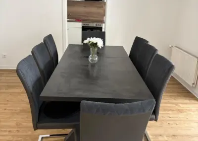 Esszimmertisch aus schwarzem Material mit sechs grauen Stühlen, dekoriert mit einer Vase und weißen Blumen.