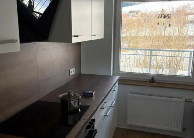 Moderne Küche mit Holzarbeitsplatte, Kochfeld und Fenster, das Tageslicht hereinlässt.