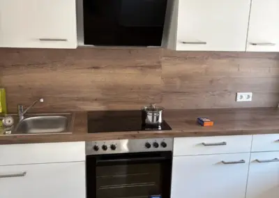 Moderne Küche mit weißen Schränken, einem schwarzen Herd und einer Dunstabzugshaube, sowie einem Edelstahlspülbecken.