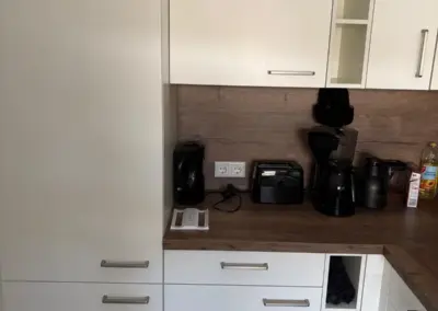 Moderne Küche mit weißen Schränken und Holzarbeitsplatte, ausgestattet mit Kaffeemaschinen und weiteren Küchengeräten.