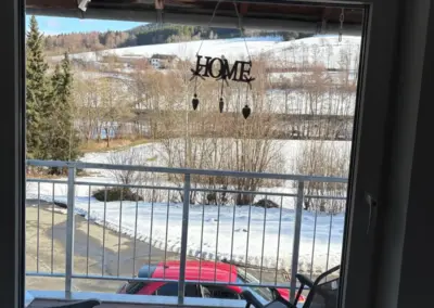 Fenster mit Blick auf eine verschneite Landschaft und einem Schild mit der Aufschrift 'HOME'.