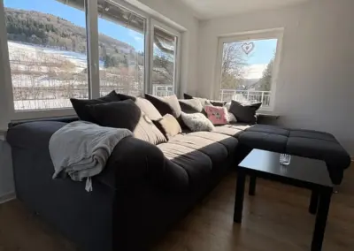 Grauem Sofa mit Kissen in einem hellen Raum mit großen Fenstern und Blick auf die Landschaft.