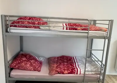 Etagenbett mit silbernem Metallrahmen und roten Bettwäsche-Sets in einem hellen Raum.