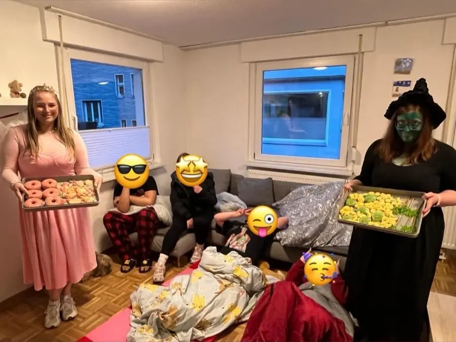 WG-Übernachtungsparty in der Feidikstraße: Freundinnen tragen Backbleche voller bunter Kekse und Donuts, im Wohnzimmer liegen Decken, fröhliche Stimmung inklusive Wicked