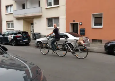 Ein Mann fährt auf einem Tandemfahrrad durch eine enge Wohnstraße mit geparkten Autos und Mehrfamilienhäusern während des autofreien Monats.
