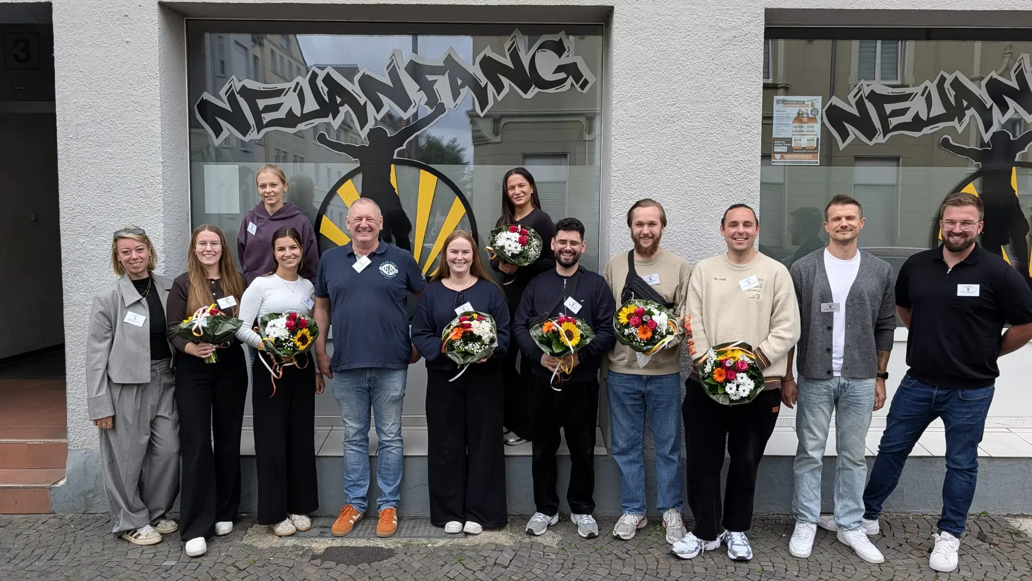 Mitarbeitende von Neuanfang Hamm stehen mit Blumen vor dem Eingang der Kinder- und Jugendhilfe in Hamm.