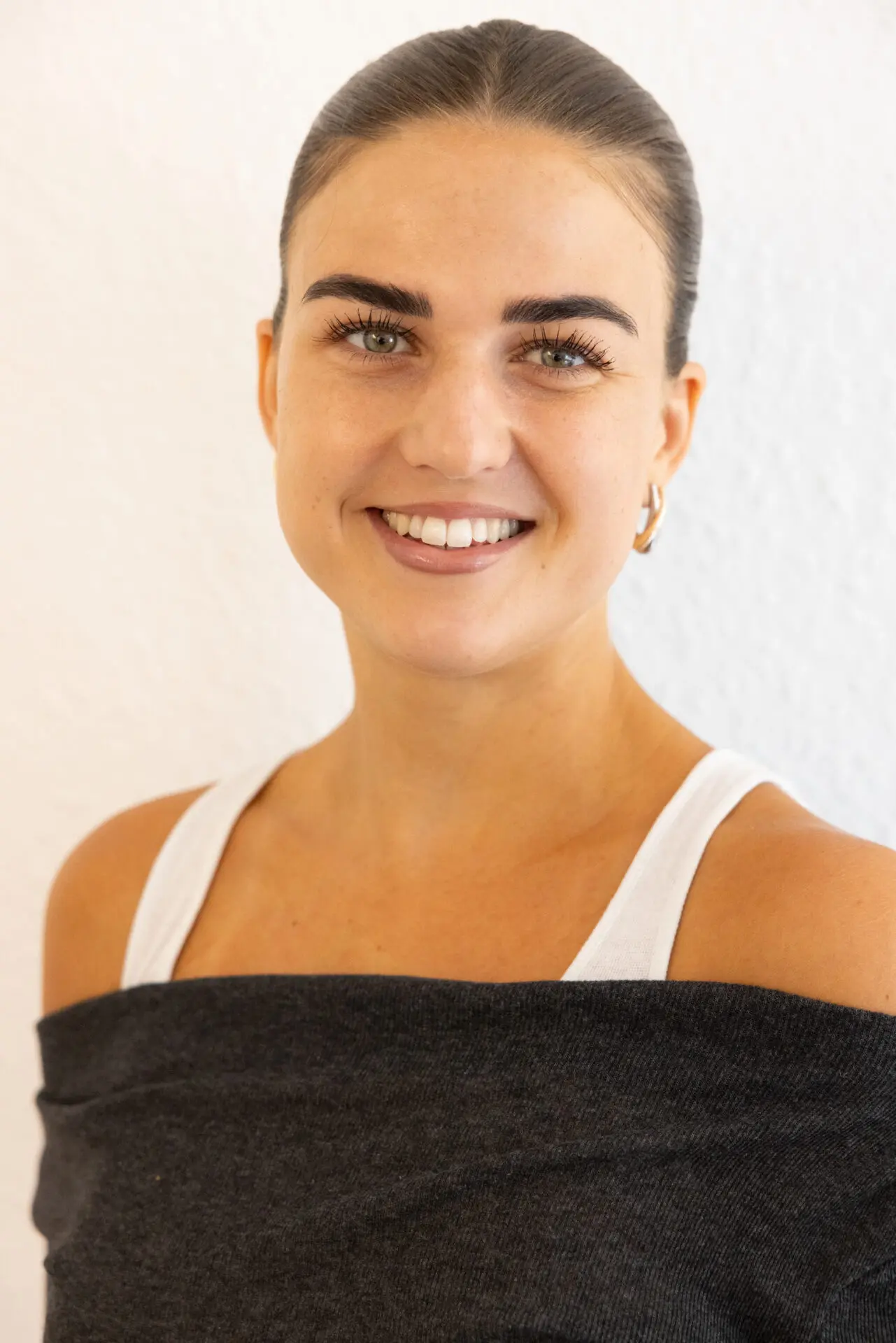 Rosalie Tiggemann lächelt freundlich in die Kamera und trägt ein weißes Oberteil mit dunklem Tuch vor hellem Hintergrund.