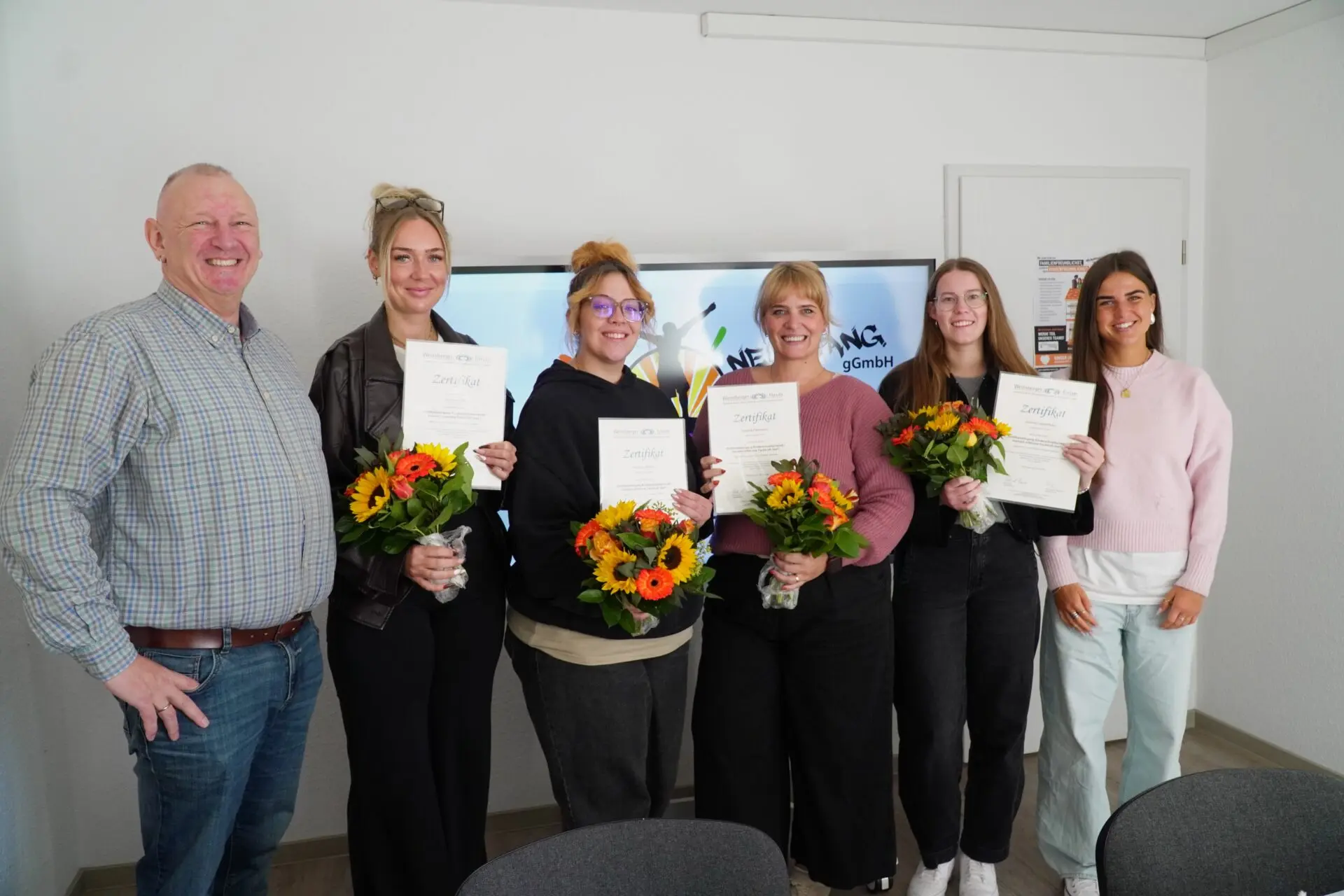 Bei Neuanfang Hamm freuen sich fünf Mitarbeiterinnen mit Zertifikaten und bunten Blumensträußen über einen erfolgreichen Neuanfang.